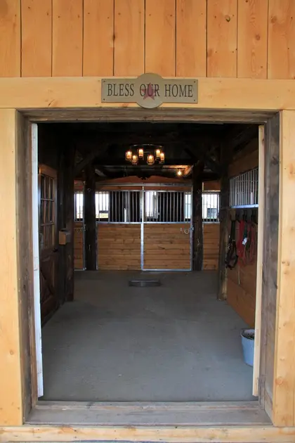 Entrée d’écurie donnant sur des box pour chevaux en bois et métal Equinad.